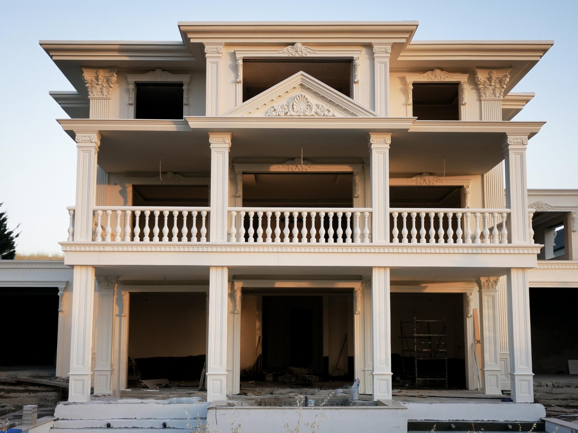 Gün ışığında üç katlı neoklasik malikanenin dış cephesinde kare sütunlar, balustrad balkon ve üçgen söve alınlığı.