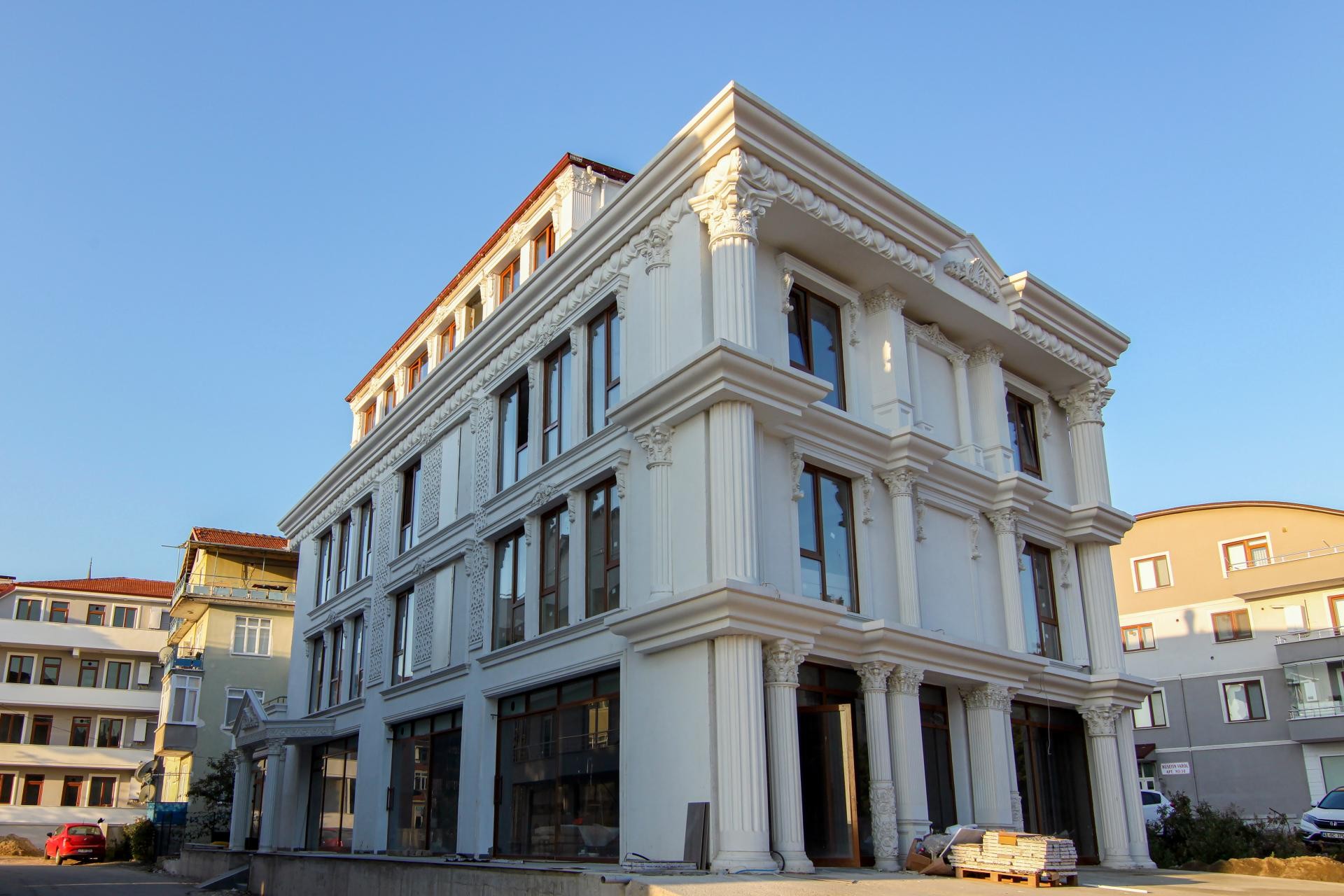 Dört katlı klasik beyaz binanın köşe cephesinde yivli sütunlar, desenli cephe panelleri ve kat silmeleri.