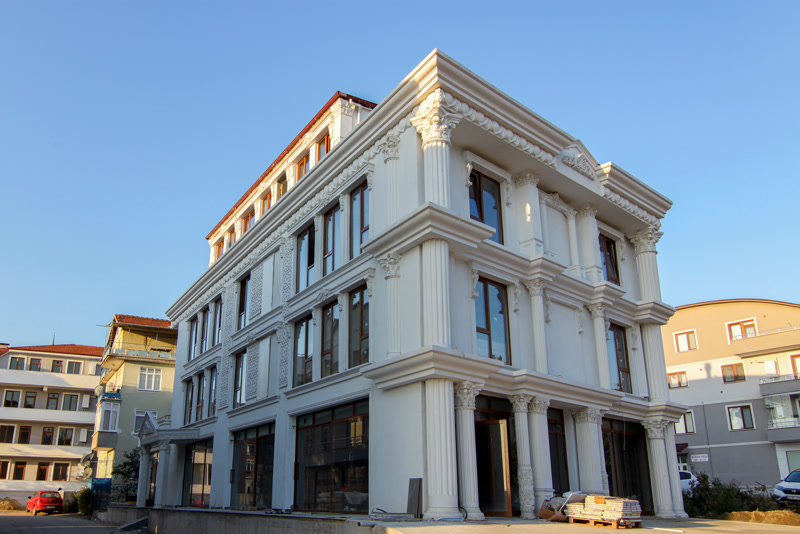 Dört katlı klasik beyaz binanın köşe cephesinde yivli sütunlar, desenli cephe panelleri ve kat silmeleri.