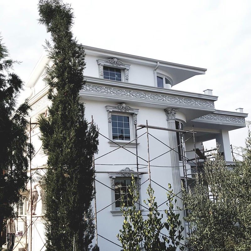 İskele kurulu beyaz villa cephesinde oymalı taçlı pencere söveleri, kat silmeleri ve sütun uygulaması.