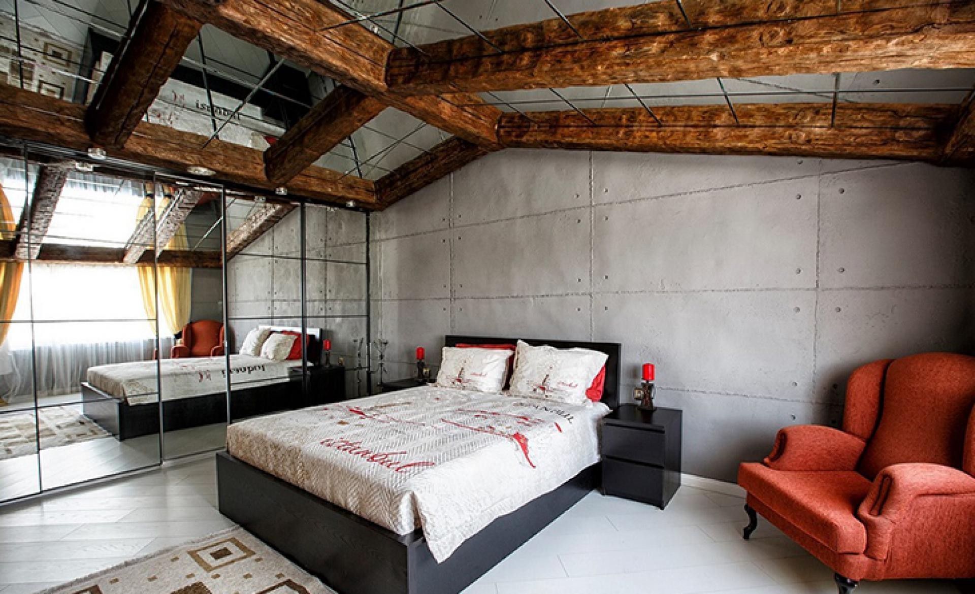 Loft yatak odasında brüt beton duvar, ahşap tavan kirişleri, kırmızı berjer ve beyaz poliüretan süpürgelik