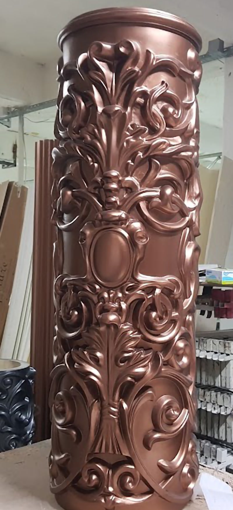 Atölye ortamında sergilenen metalik bronz boyalı, oval madalyon ve barok akantüs oymalı poliüretan dairesel sütun gövdesi kaplaması
