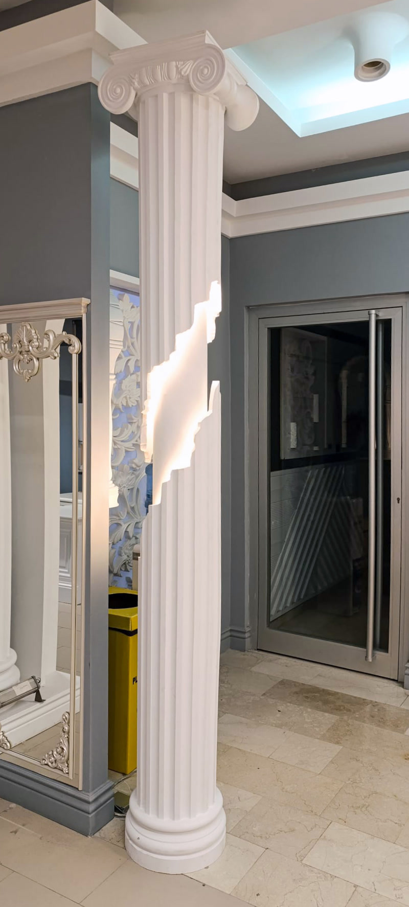 Showroom girişinde aydınlatmalı yivli poliüretan İyon sütun, gümüş oymalı ayna çerçevesi sövesi ve cam kapı.