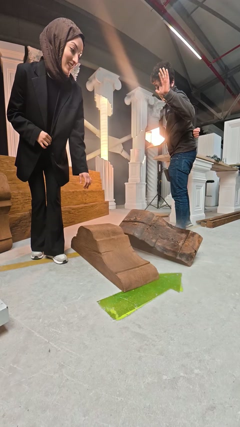 İki görevli, atölye zeminindeki kahverengi dekoratif parçaları hareketle tanıtıyor.