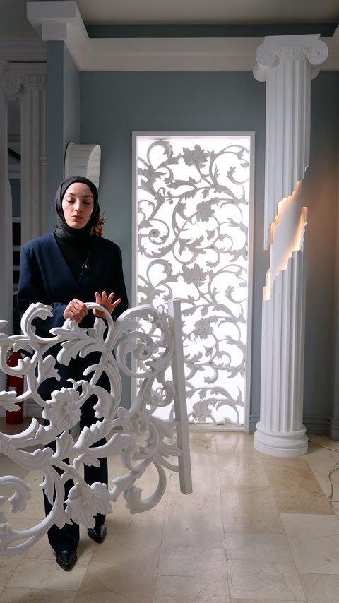 Sütunlu salonda görevli, kıvrımlı beyaz panel parçasını önünde tutuyor