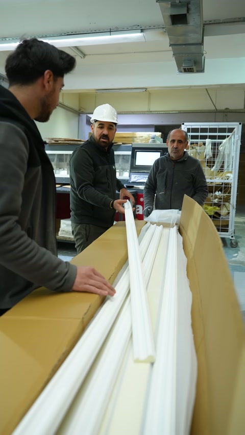 Üç görevli, kutudaki poliüretan çıtaların dizilimini birlikte kontrol ediyor.