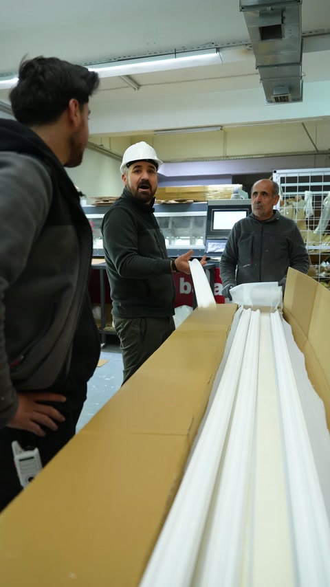 Çalışanlar, uzun dekoratif çıtaları paketleme masasında inceliyor.