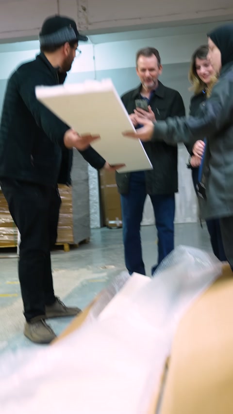 Üç kişi, atölyede elde tutulan geniş panel yüzeyini değerlendiriyor.