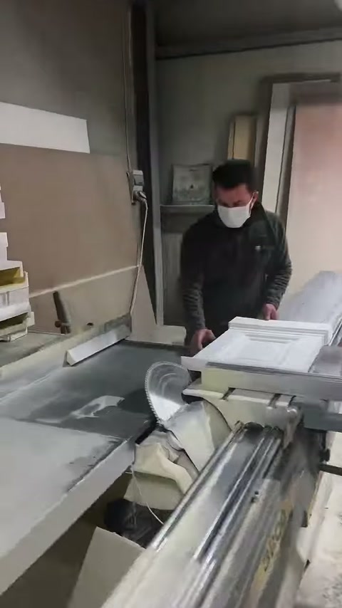 Maskeli usta, beyaz dekoratif profilleri kesim makinesine yerleştiriyor.