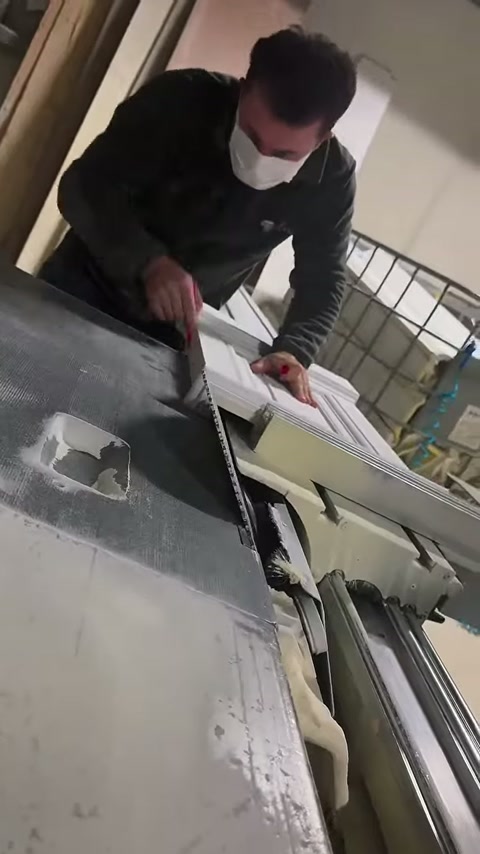 Usta, profilli beyaz parçayı testere tablasında iki eliyle sabitliyor.