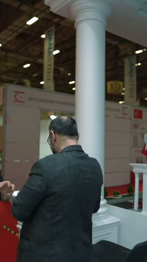 İki ziyaretçi, standdaki büyük dekoratif sütunların yanında sohbet ediyor