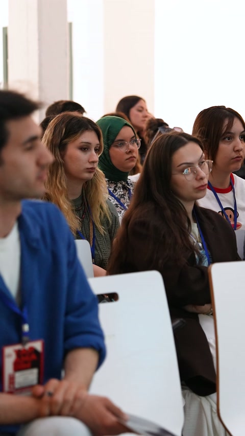 Katılımcılar, beyaz sandalyelerde oturarak teknik sunuma odaklanıyor