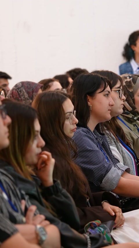 Salondaki genç katılımcılar konuşmacıyı yan profilden izliyor
