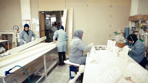 Beyaz önlüklü çalışanlar uzun üretim tezgâhında parçaları hazırlıyor.
