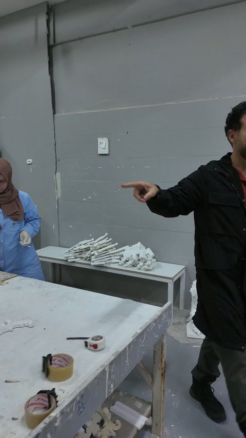 Usta, üretim tezgâhını ve çevredeki tamamlanmış parçaları işaret ediyor.