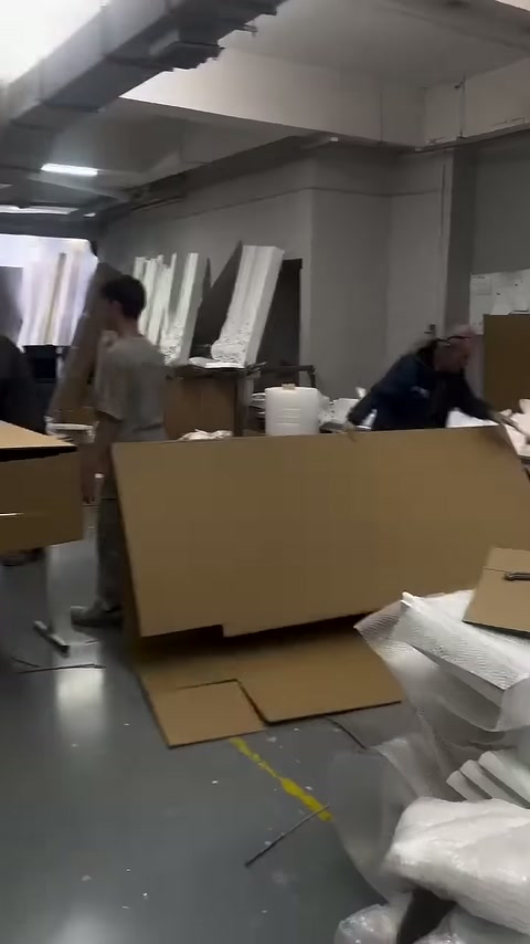 Çalışanlar büyük karton kutunun kenarlarını karşılıklı olarak kaldırıyor