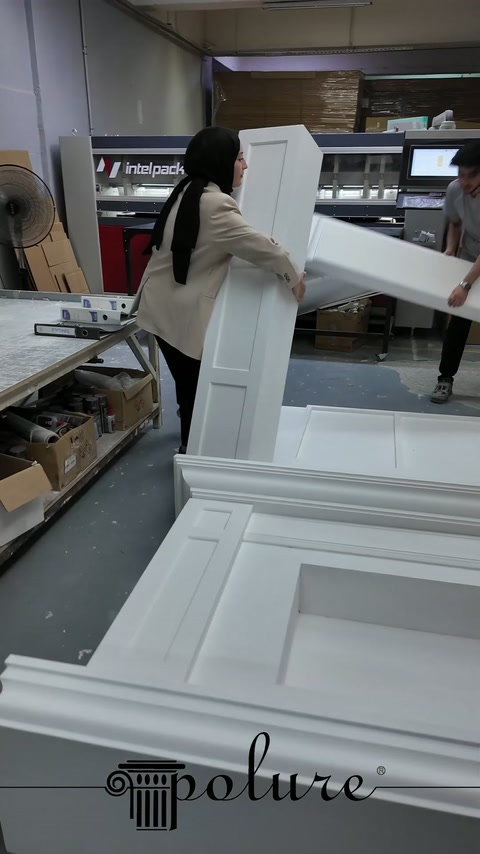 Geniş beyaz şömine paneli atölyede dik konumda taşınıyor.