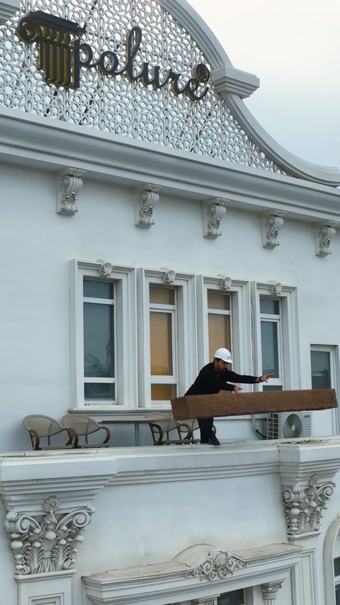 Baretli uygulayıcı beyaz binanın balkonunda uzun dekoratif kirişi taşıyor.