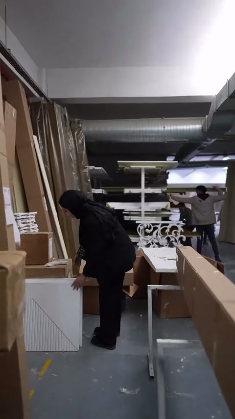 Atölye geçidinde kutular, uzun profiller ve iş masaları sıralanıyor.