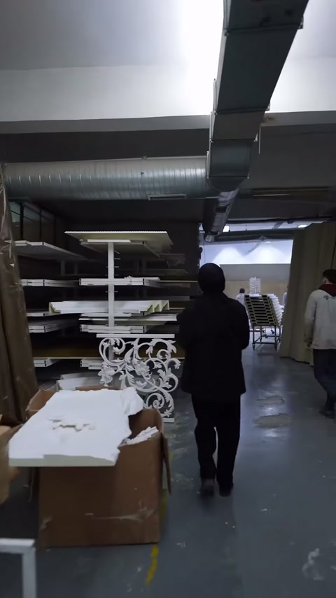 Sunucu, geniş atölyede beyaz oyma panel sergisine yaklaşıyor.