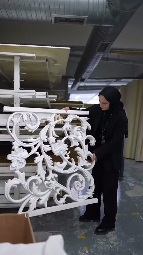 Sunucu, yoğun bitkisel desenli korkuluk panelinin yanında duruyor.