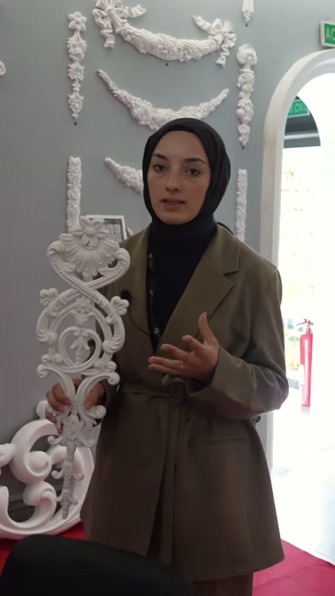 Büyük beyaz bezeme, klasik desenli sergi duvarı önünde sunuluyor