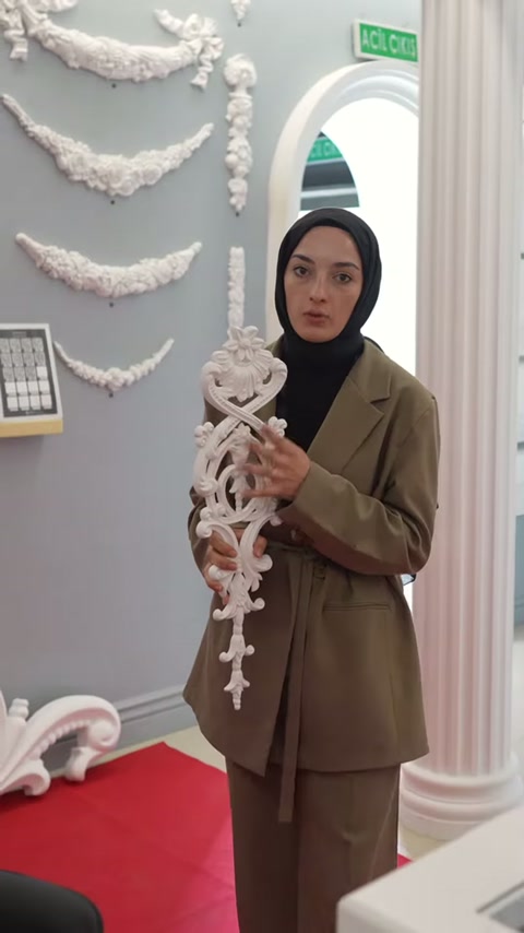 Çiçekli kıvrımlara sahip beyaz motif pembe sütun yanında sergileniyor