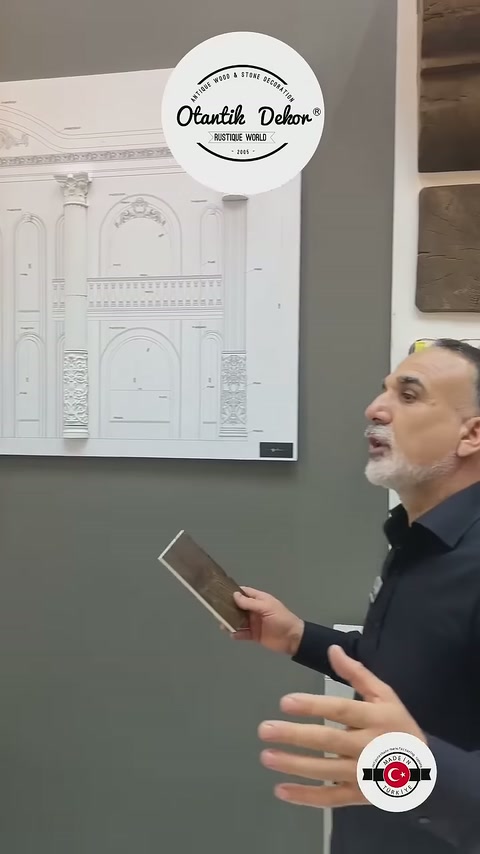 Görevli çizim panosu yanında elindeki kahverengi kaplama parçasını gösteriyor