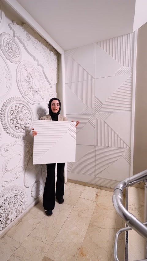 Kare kabartmalı panel, tamamlanmış geometrik duvar önünde elde tutuluyor