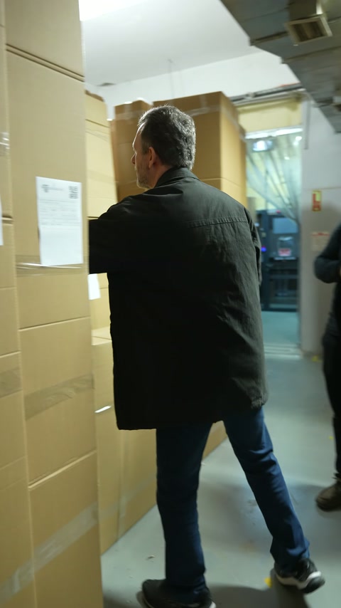 Müşteri, fabrika deposundaki uzun karton paketlere doğru ilerliyor.