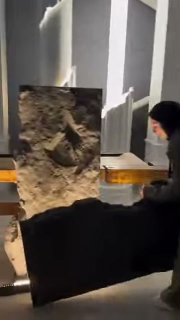 Koyu renkli panel parçası, kabartılı kaya panelin önünde yatay tutuluyor