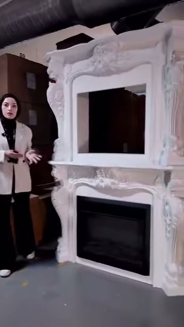 Beyaz şömine çevresindeki kıvrımlı motifler depo ışığında belirginleşiyor