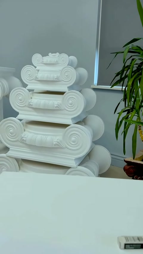 Beyaz İyon sütun başlıklarının volütlü modelleri masa arkasında sıralanıyor.