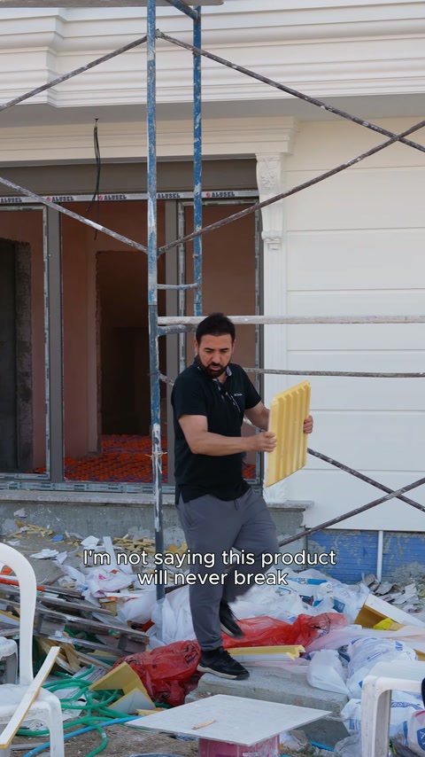 Sunucu, şantiye önünde sarı oluklu kaplama numunesini elinde tutuyor.