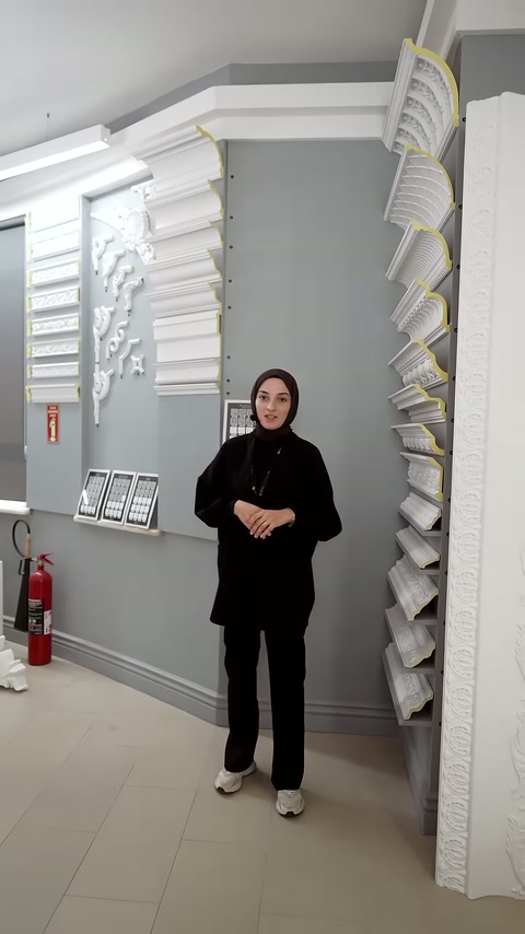 Showroomda sunucu, duvara monte farklı kartonpiyer kesitleri önünde konuşuyor.