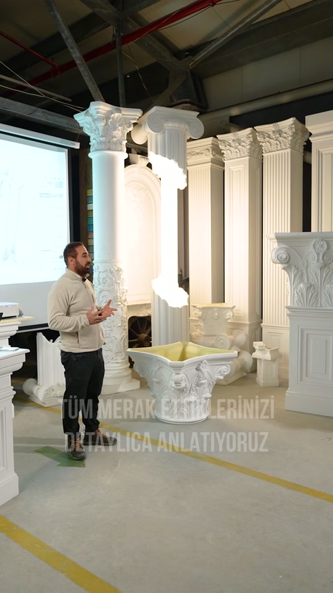Sunucu, yüksek sütunların ve süslü kaidelerin bulunduğu showroomda ilerliyor.