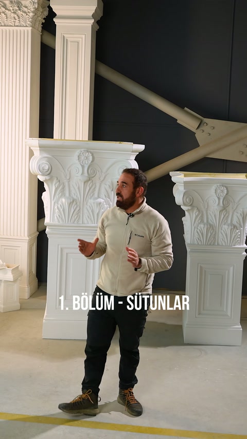 Sunucu, korint başlıklı uzun sütun örneklerinin önünde açıklama yapıyor.