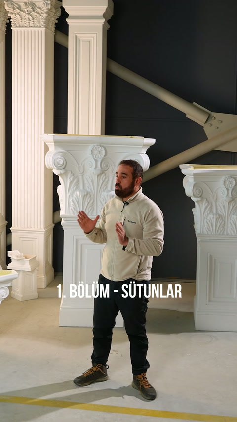 Sunucu, yivli sütun gövdeleri ve bezemeli başlıklarla çevrili alanda konuşuyor.